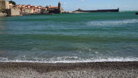 waves slowly hitting the beach in collioure with the old town in the background on a hot bright windy day, france