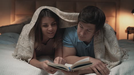 pareja joven leyendo, cubierta con una manta