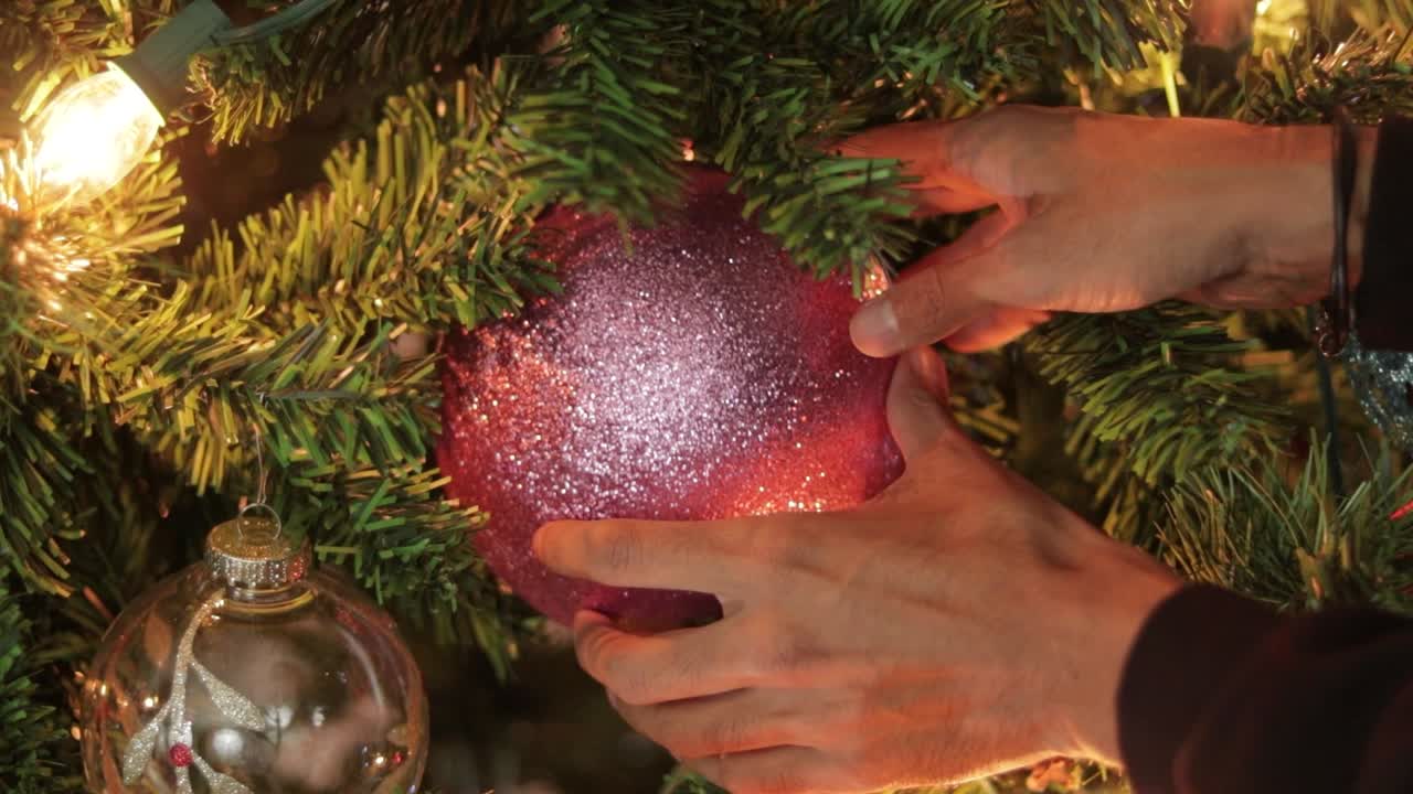 colocando una gran pelota de navidad de brillo rosa en un árbol de navidad decorado