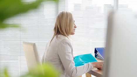 Businesswoman-holding-file-and-mobile-phone-at-her-desk