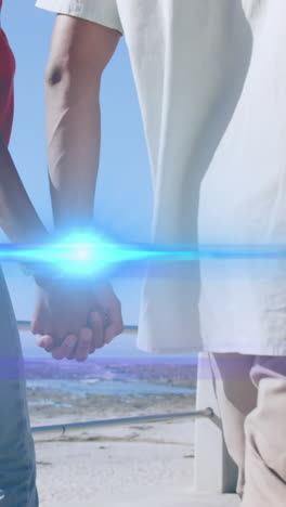 animation of light moving over midsection of couple walking by beach holding hands