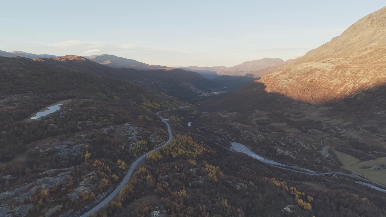 A drone video showcasing a winding road through autumn-colored mountains, gently lit by the sun in Jotunheimen National Park