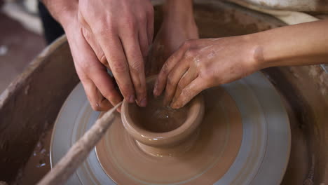 close up of male teacher helping woman sitting at wheel in pottery class