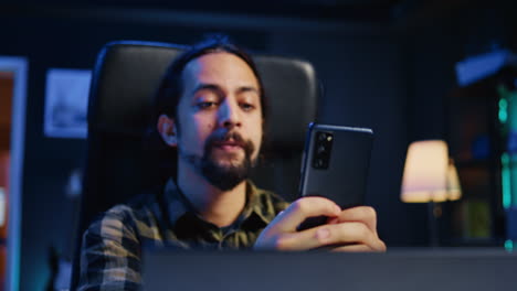 hombre feliz en casa enviando mensajes de texto a un amigo en el teléfono móvil, tomando un descanso del trabajo remoto