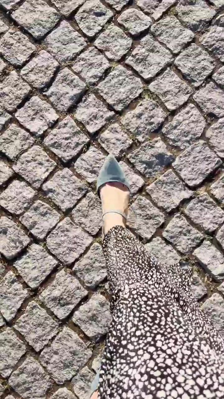Elegantly dressed woman POV feet with high heels walking on cobblestone street in Europe. Female tourist or local enjoying hot summer or spring day outdoors. Walking happily during vacation. UGC reel