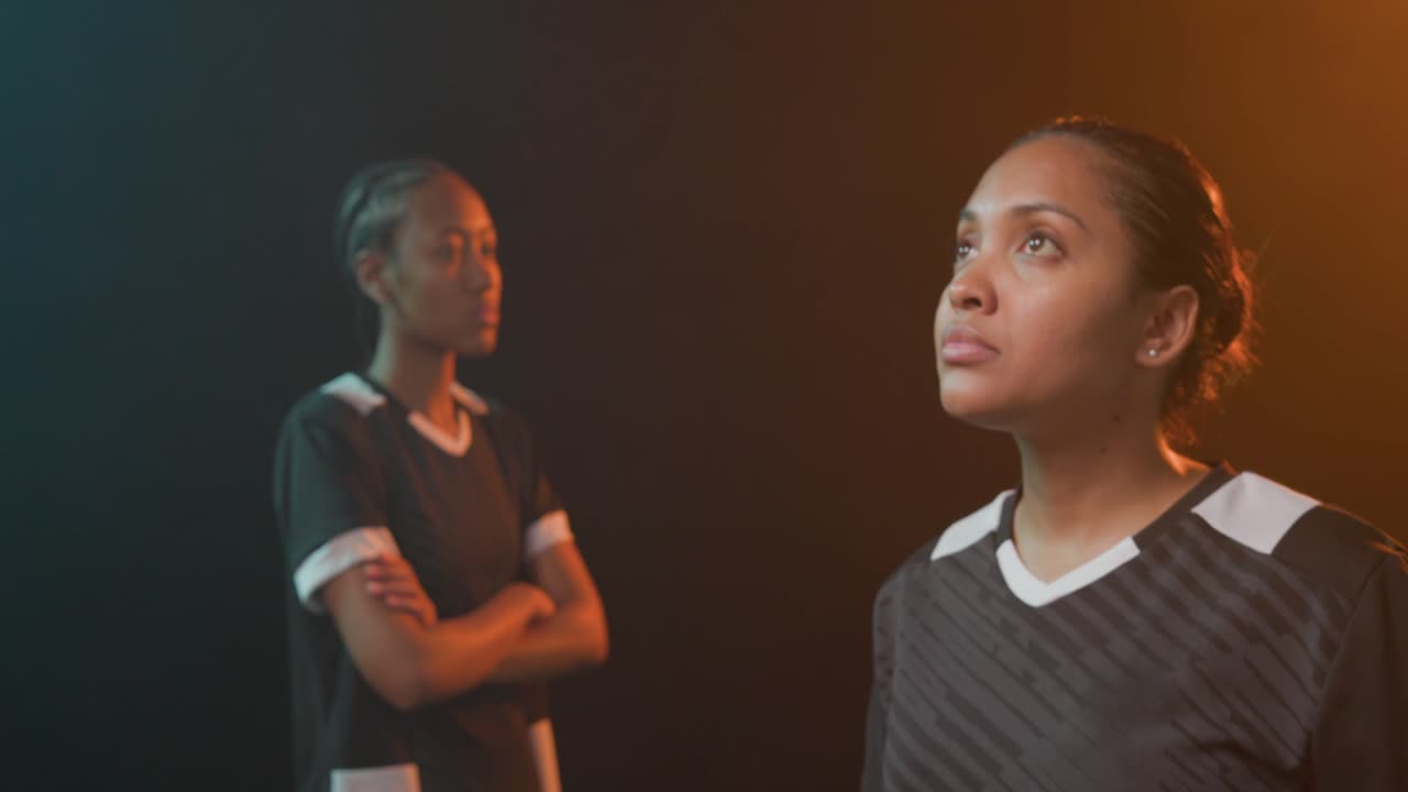 Duo femminile afroamericano che posa in divisa tenendo un pallone da calcio, con l'obiettivo che si allarga sotto un bordo verde acqua e ambra.
