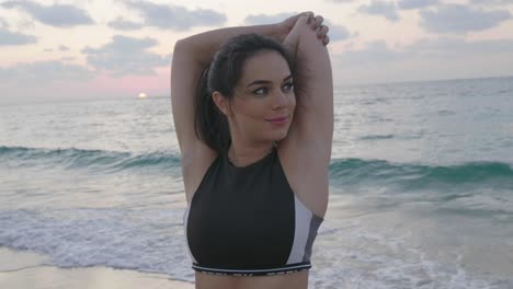 atractiva mujer morena entrenando en la playa durante la puesta de sol