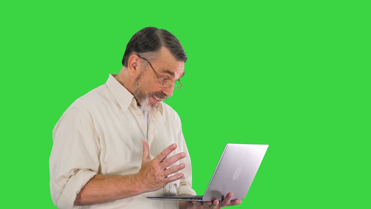 hombre maduro con gafas feliz de terminar el trabajo en la computadora portátil a tiempo en una pantalla verde, llave de croma