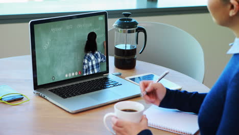 Caucasian-female-student-using-laptop-on-video-call-with-female-teacher,-making-notes