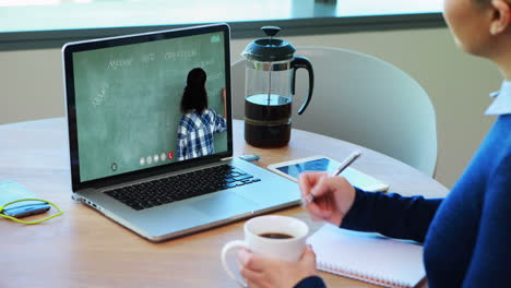 estudiante caucásica usando una computadora portátil en una videollamada con una maestra, tomando notas