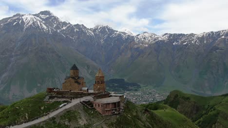 drone aerial view in georgia flying by gergeti trinity medieval orthodox church in kazbegi surrounded by green mountains valley with snowed peaks