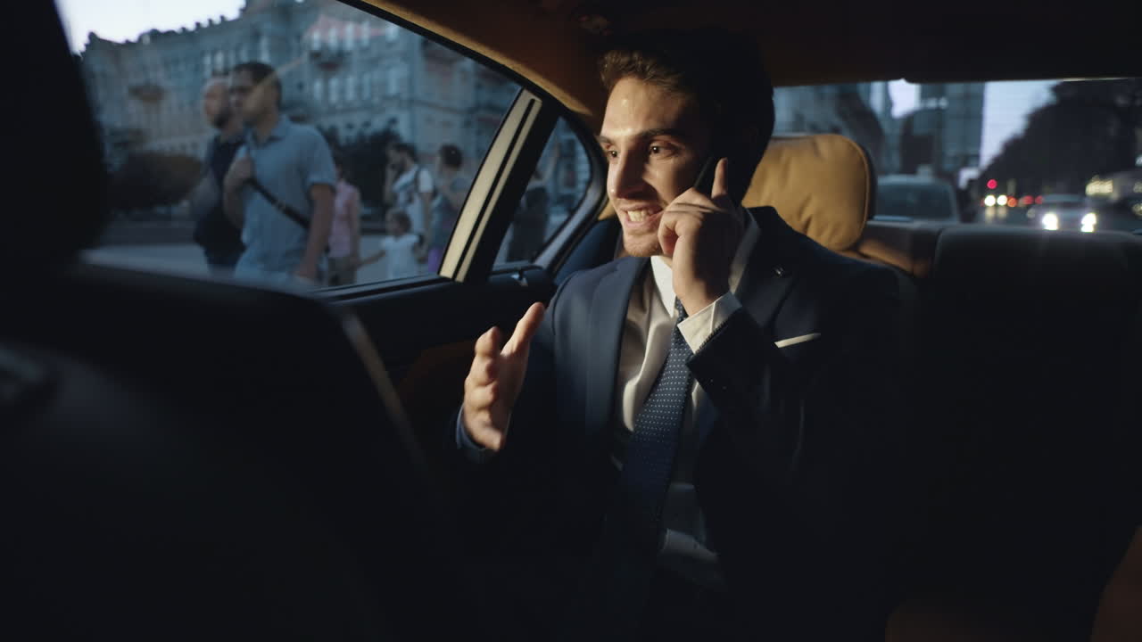 Uomo d'affari felice che condivide buone notizie sullo smartphone in un'auto aziendale scura