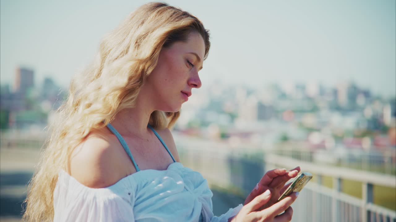 Giovane donna bionda che usa lo smartphone all'aperto con sfondo urbano