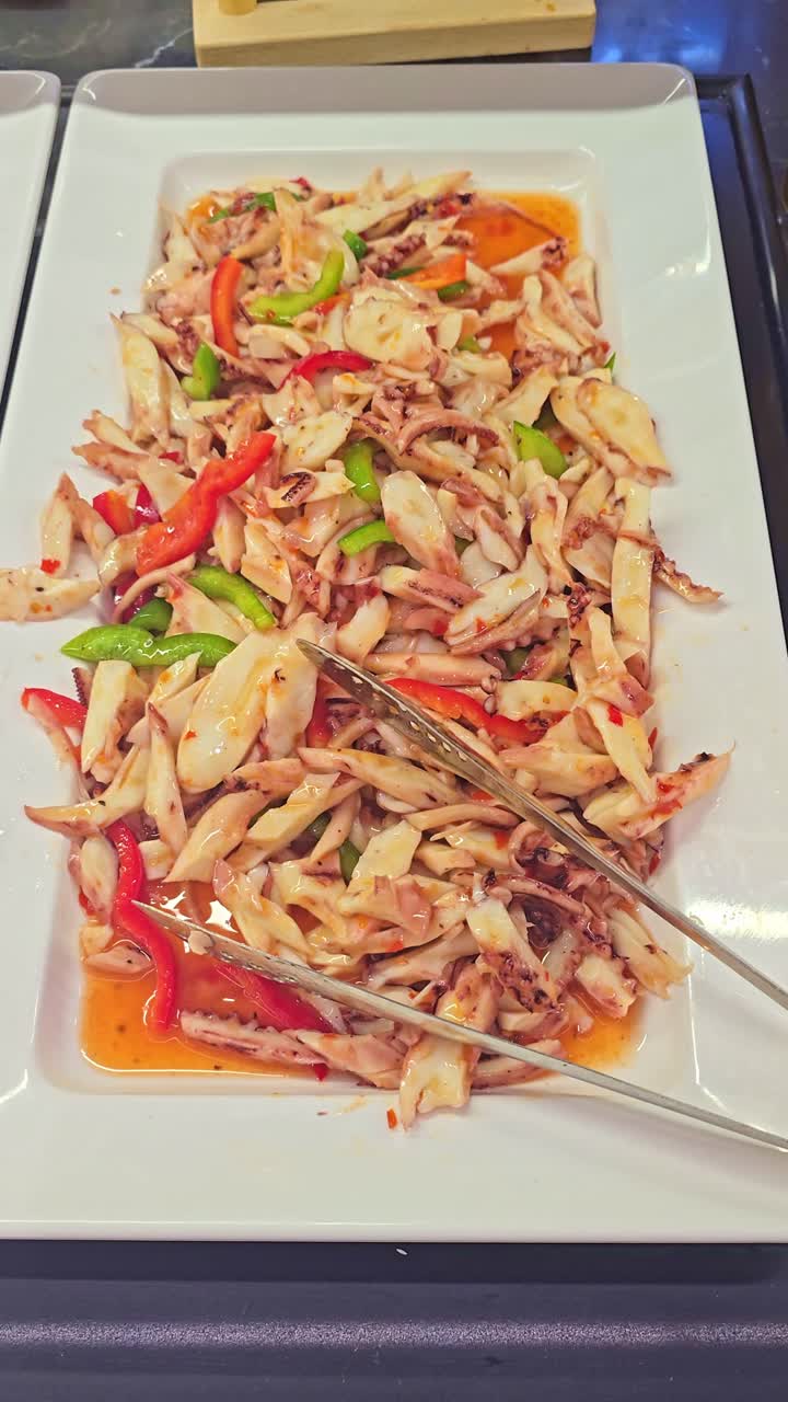 Camera slowly moves closer to a pasta salad with bell peppers and squid tentacles displayed on a buffet table in a restaurant