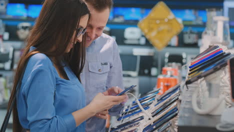 A-married-couple-standing-near-showcase-with-smartphones-in-the-modern-electronics-store-and-choose-a-new-smartphone.-Buy-a-mobile-phone