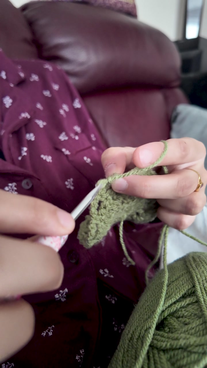 Hands working with a crochet hook and green yarn, creating textile fabric. vertical video