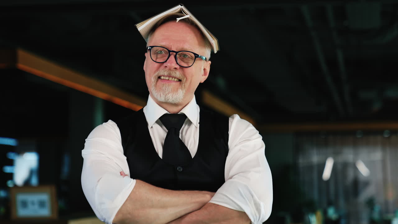 Adult man wearing glasses puts the paper notebook on his head. Businessman fooling around in office. Close up.