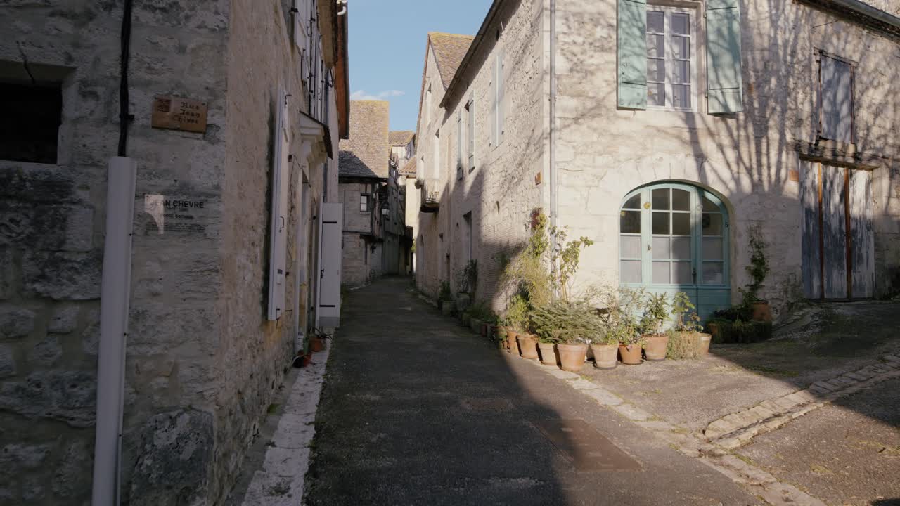 Piante in vaso e facciate in pietra con persiane lungo una stradina tranquilla nella Bastide medievale di Issigeac, Dordogna. La luce del giorno illumina lo stretto passaggio residenziale.