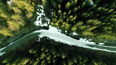 Toma-Aérea-De-Arriba-Hacia-Abajo-Sobre-Una-Carretera-Cubierta-De-Nieve-Al-Lado-Del-Bosque-De-Coníferas-Nevado-De-Invierno-En-Noruega-Durante-El-Día