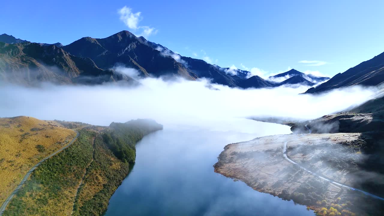 Aerial view of fog rolling over Moke Lake, surrounded by mountains in Queenstown, New Zealand. Bright daylight enhances the serene atmosphere