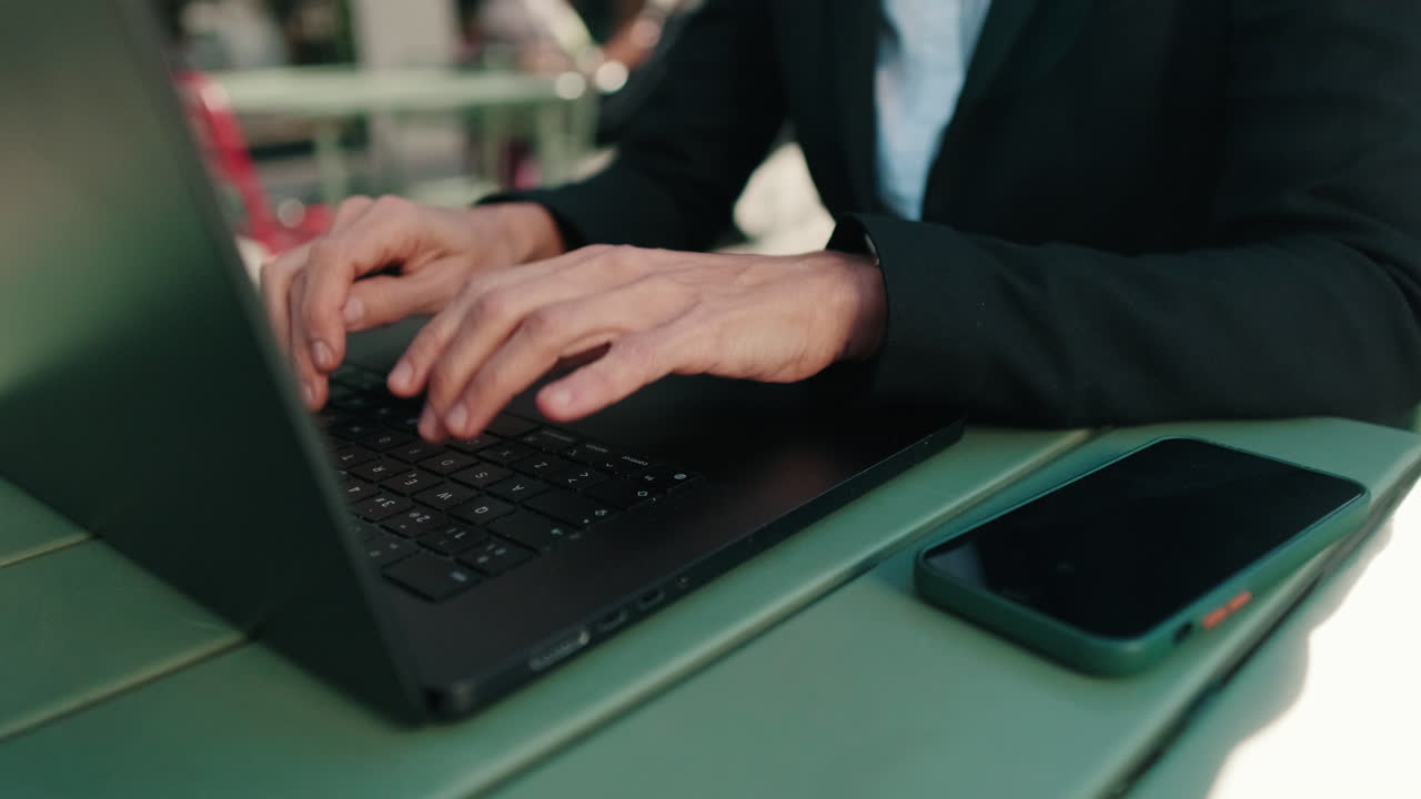 Primo piano delle mani di una persona che digita sul laptop a un tavolo all'aperto