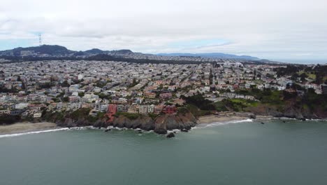 imágenes aéreas de drones de 4.000 fps de la costa de california cerca de la ciudad y la playa de presidio: olas rompiendo contra los acantilados de la costa, playa de arena, cielo nublado, olas blancas y árboles de hoja perenne salpican el paisaje