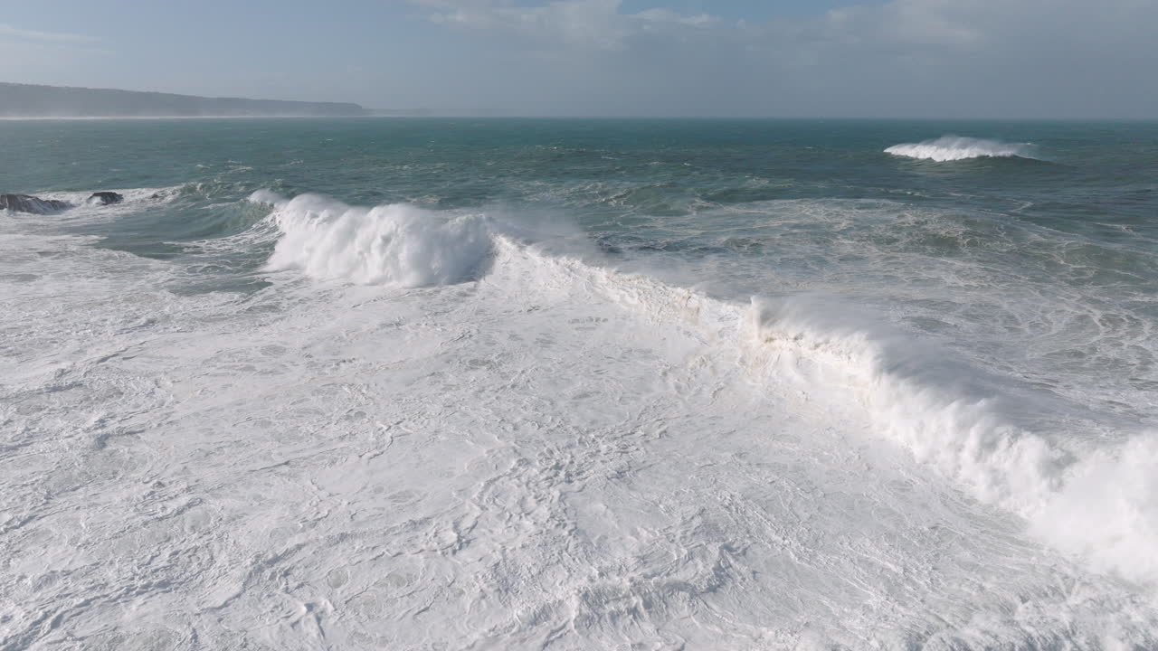 Aerial drone shot of big waves coming into shore on a day with giant waves in Nazaré, Portugal, Europe. View from beach. Rough tow-in surf conditions