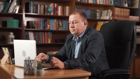 an elderly man is sitting at a table with a laptop in front of him