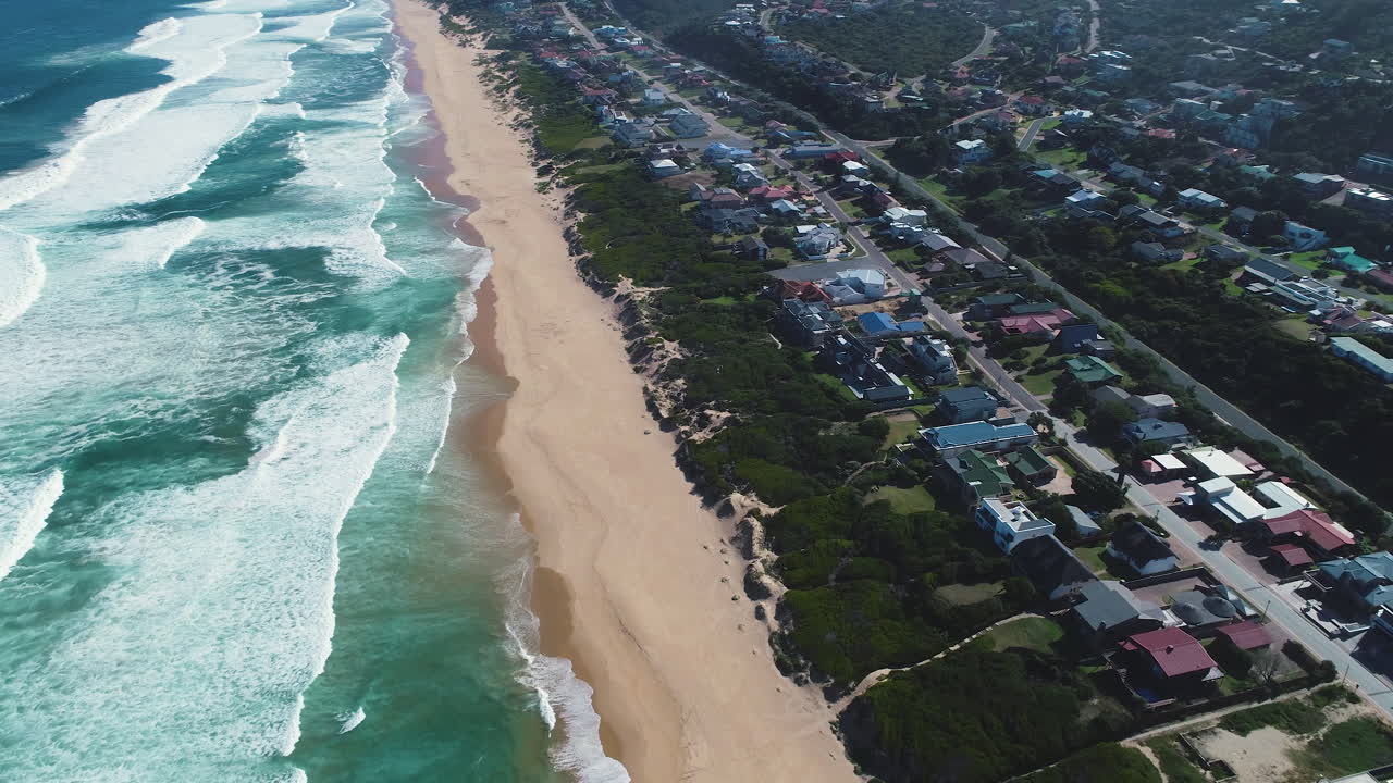 Aerial - Shot along massive stretch of pristine beach, houses behind beach dunes