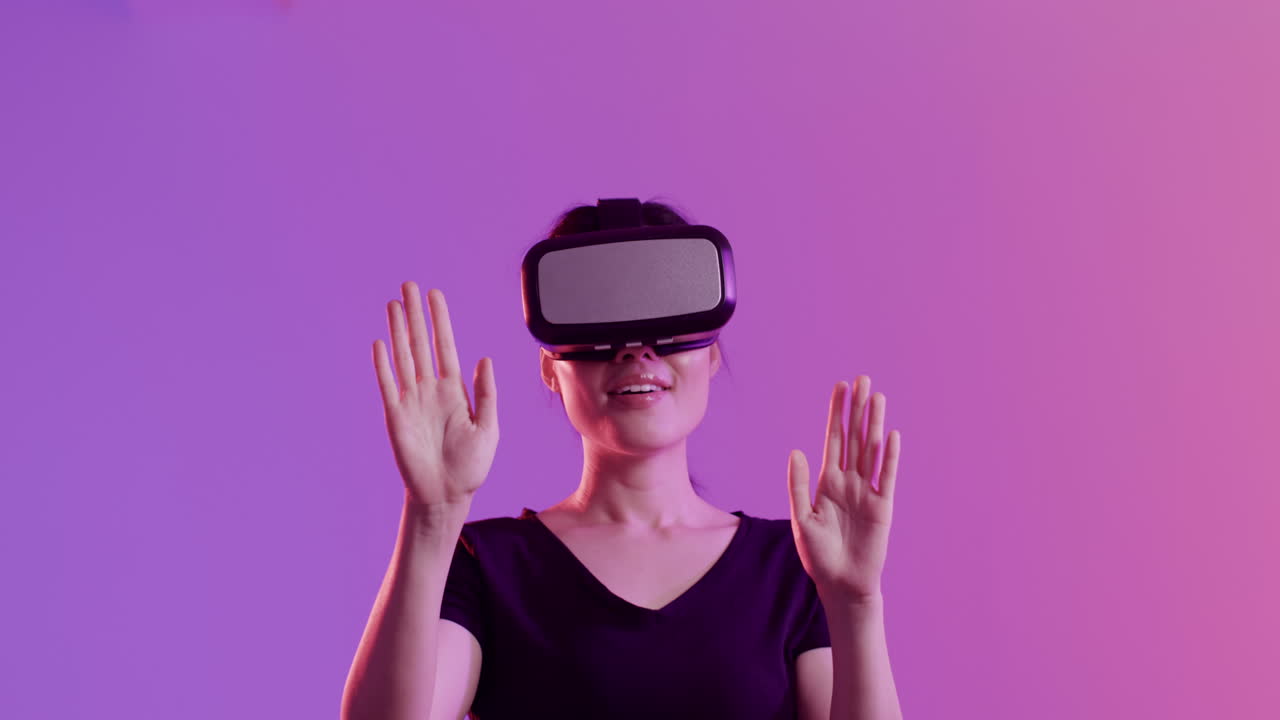Happy asian woman using vr headset and touching virtual screen on purple background, slow motion