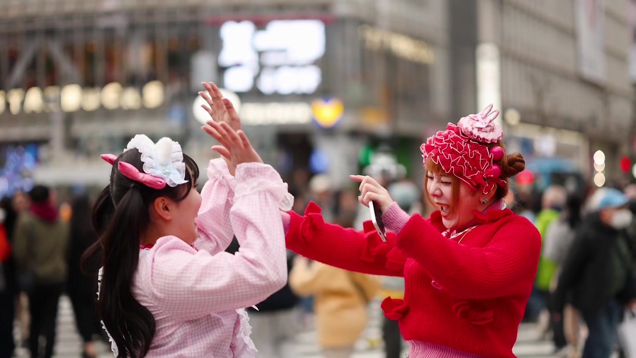 東京の原宿で、鮮やかなピンクと赤のデコラ系ストリートスタイルを身につけた2人の女性がハイタッチ