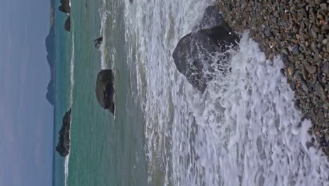 Vertical-slow-motion-shot-crashing-along-rocky-coastline-at-Banbanon-beach,-Surigao-del-Norte,-Philippines-on-a-cloudy-day