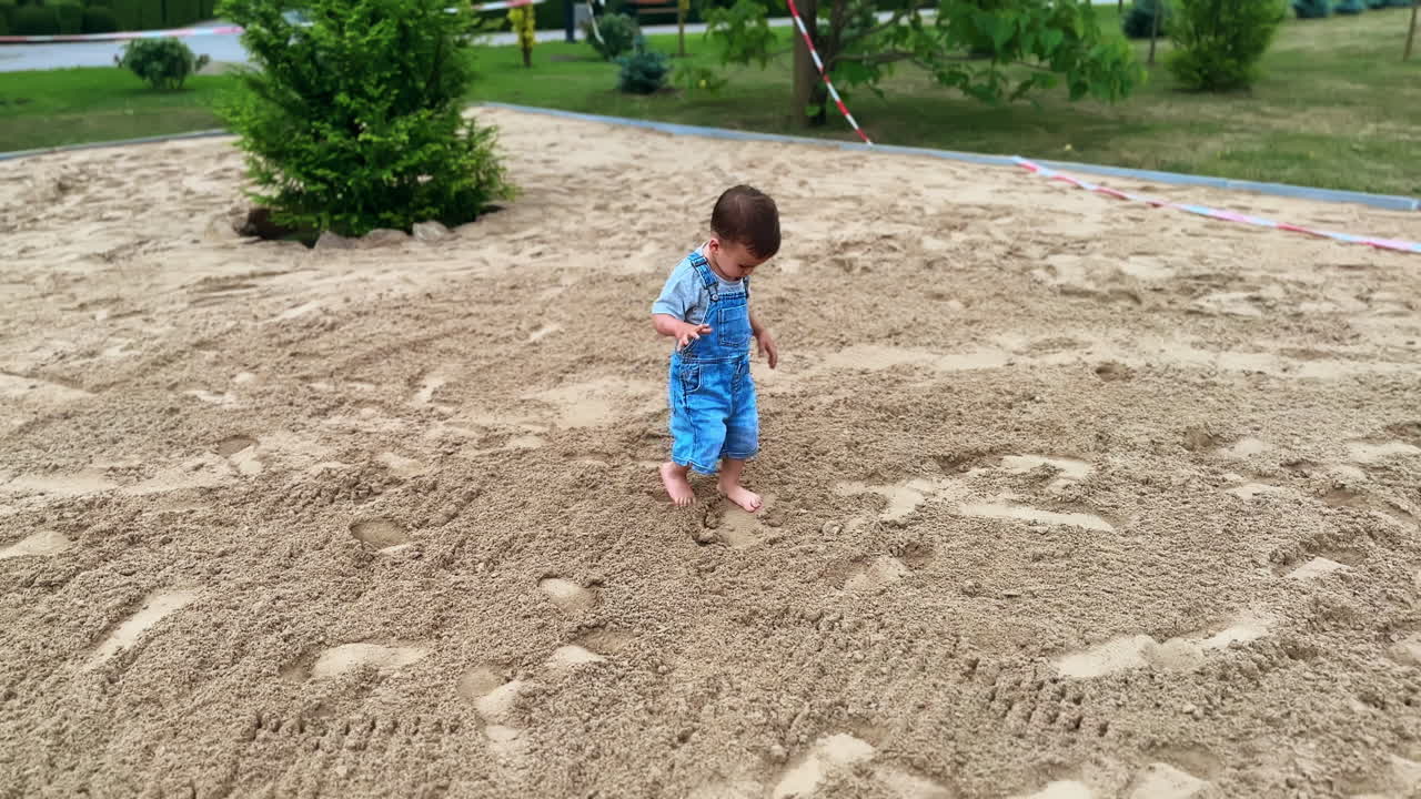 Toddler boy walks barefoot by the sand. Caucasian child in the park in summer. Top view.