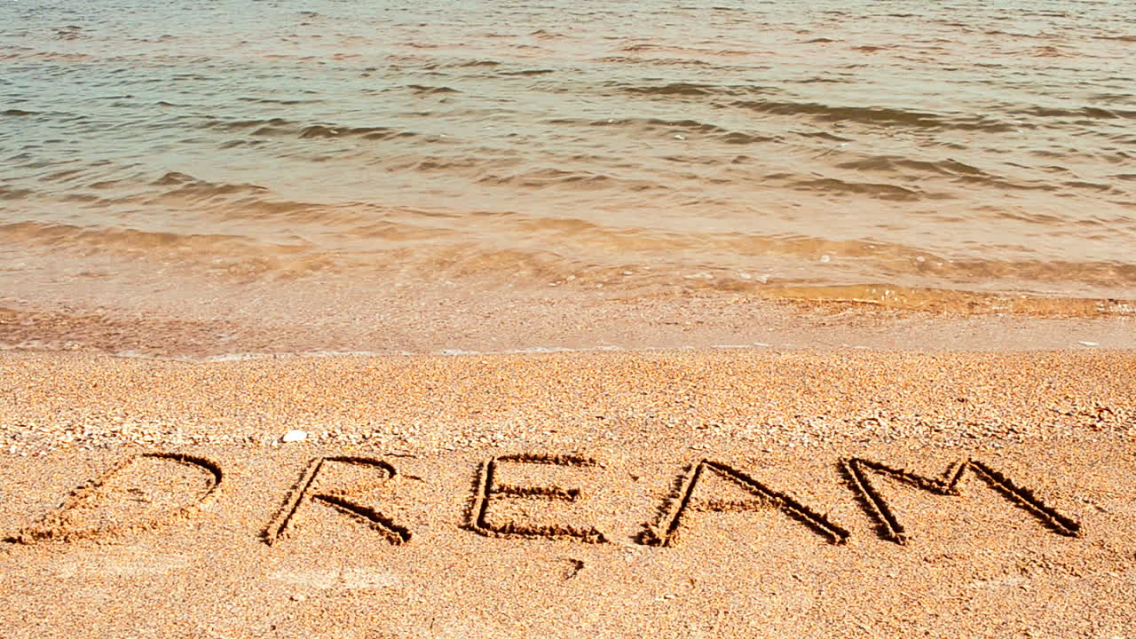 Inscription Dream on sea beach sand, with the wave. Shooting on the beach