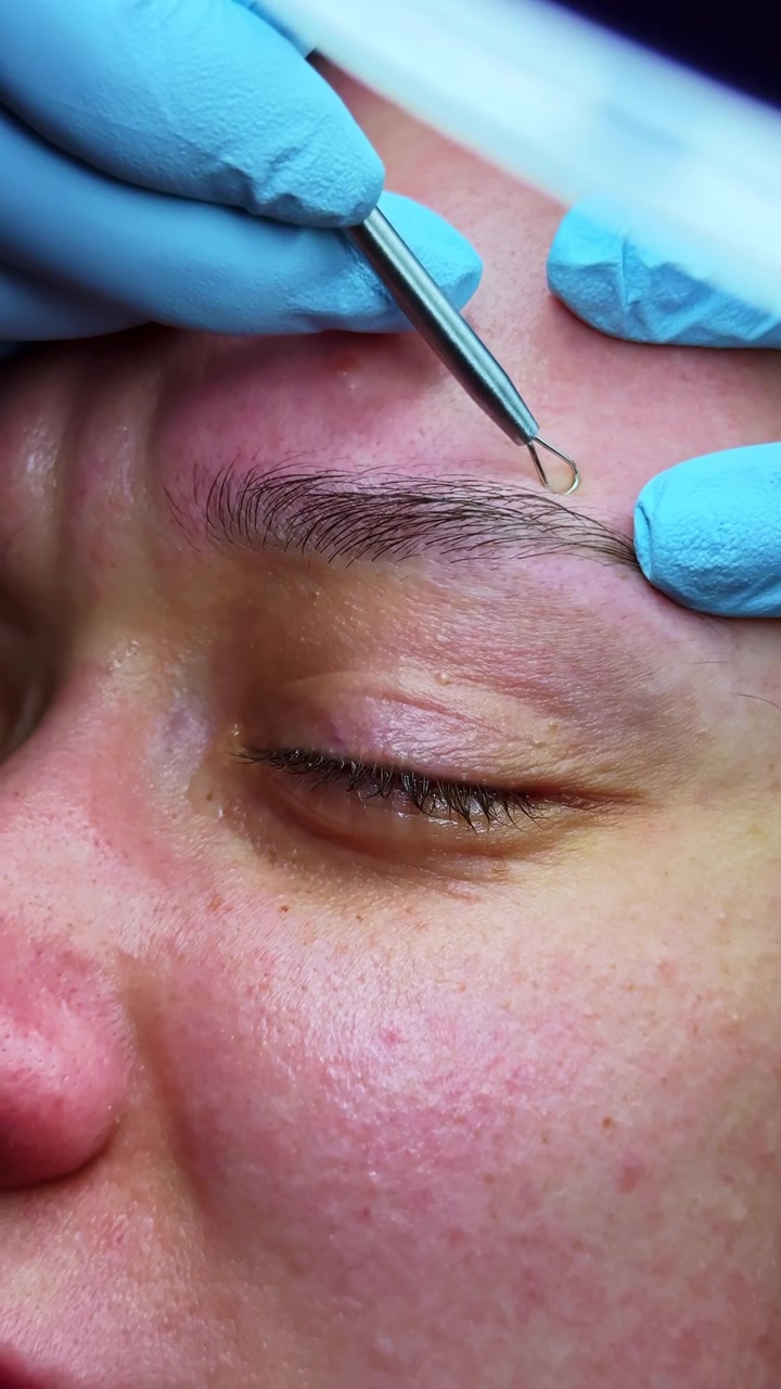 Eyebrow shaping process takes place in beauty salon during afternoon hours with a client lying down
