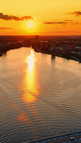 Single motor boat crossing the Charles River at sunset. Amazing scenery of Boston, Massachusetts, USA from top under orange sky. Vertical video