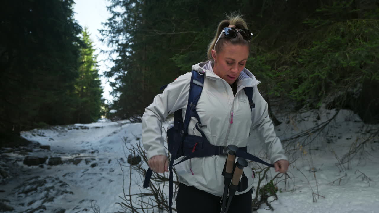 Blond caucasian woman hiking in snowy mountain and tying her backpack around her waist, gimbal shot