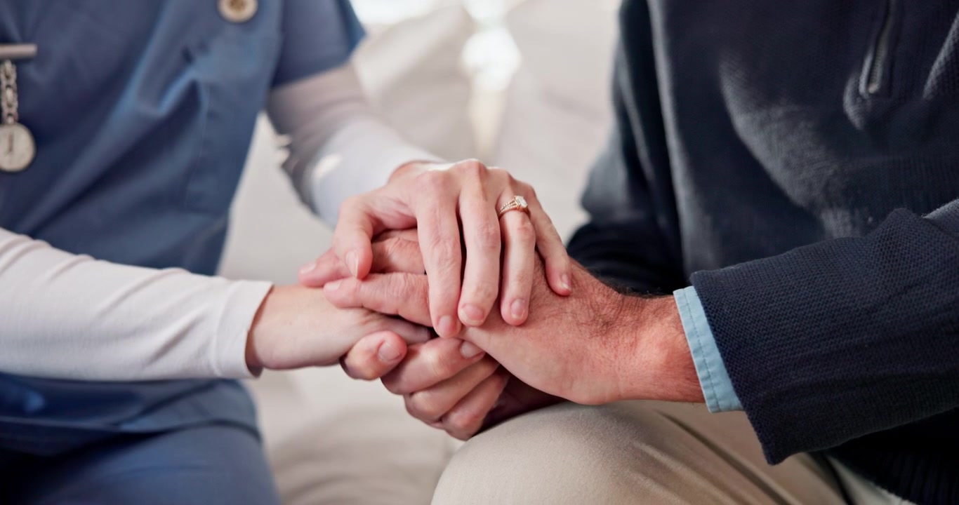Infermiera che conforta un paziente anziano tenendogli le mani