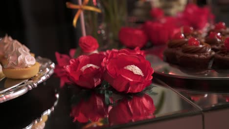 table with a variety of desserts, cupcakes and cakes, decorated with red roses