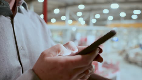 primer plano de un ingeniero de fábrica escribiendo un mensaje de texto en un teléfono móvil
