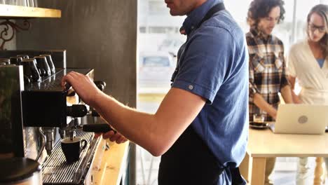 Waiter-preparing-coffee-while-couple-using-laptop