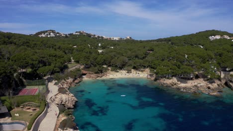 Mallorca-Cala-Gat-Beach-with-clear-blue-water-at-a-sunny-day-with-surfer-on-the-water-and-mountains-in-the-background