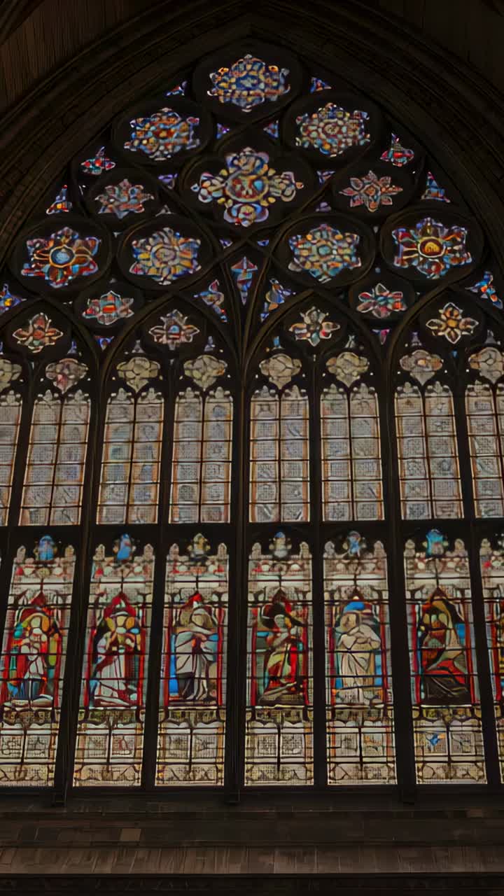 Vertical video: Panning down Gothic glass cleric in collar holding book by poles in church for mass