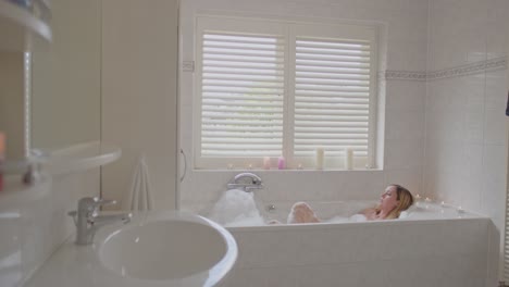 Wide-view-of-attractive-woman-enjoying-a-foam-covered-bath-in-a-beautiful-bathroom-surrounded-by-candles---dolly-out