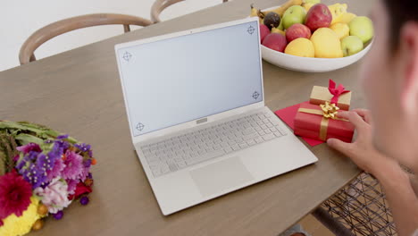 biracial man with gifts having video call on laptop with copy space on screen, slow motion