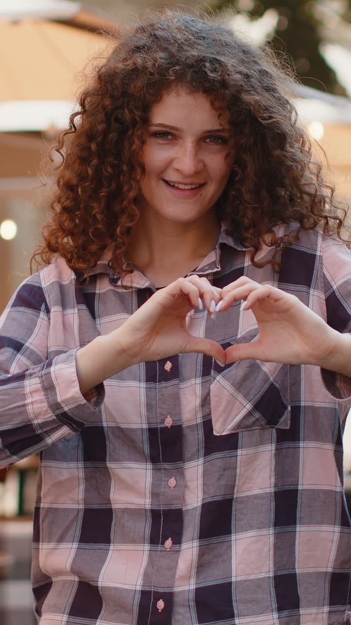Una giovane donna fa il simbolo dell'amore mostrando il segno del cuore alla telecamera per esprimere sentimenti romantici e positivi