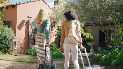 two woman friends arriving at hotel villa with trolly bags enjoying summer vacation at beautiful country house excited for holiday 4k footage