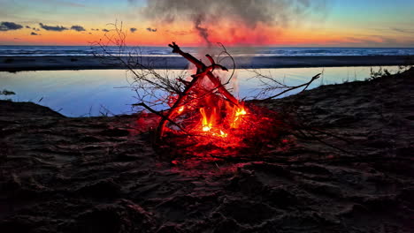 una persona agrega s palo para alimentar una fogata en la playa al atardecer - cámara lenta