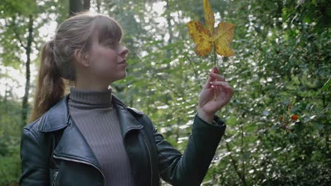 beautiful young woman holds up leaf to admire in woods, slow motion