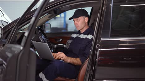 Mechanic-working-on-laptop-in-auto-repair-service-inside-the-car